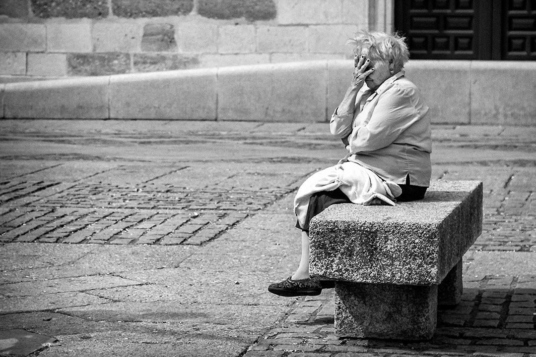 A woman seated on a bench beside a facade.